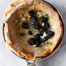 pancake on a skillet with blackberries, thyme, powdered sugar and almond flakes on top