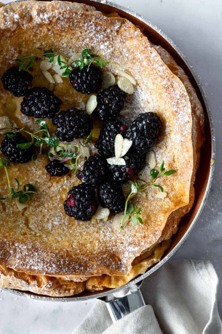 pancake close up with blackberries, thyme, flaked almonds and powdered sugar on top