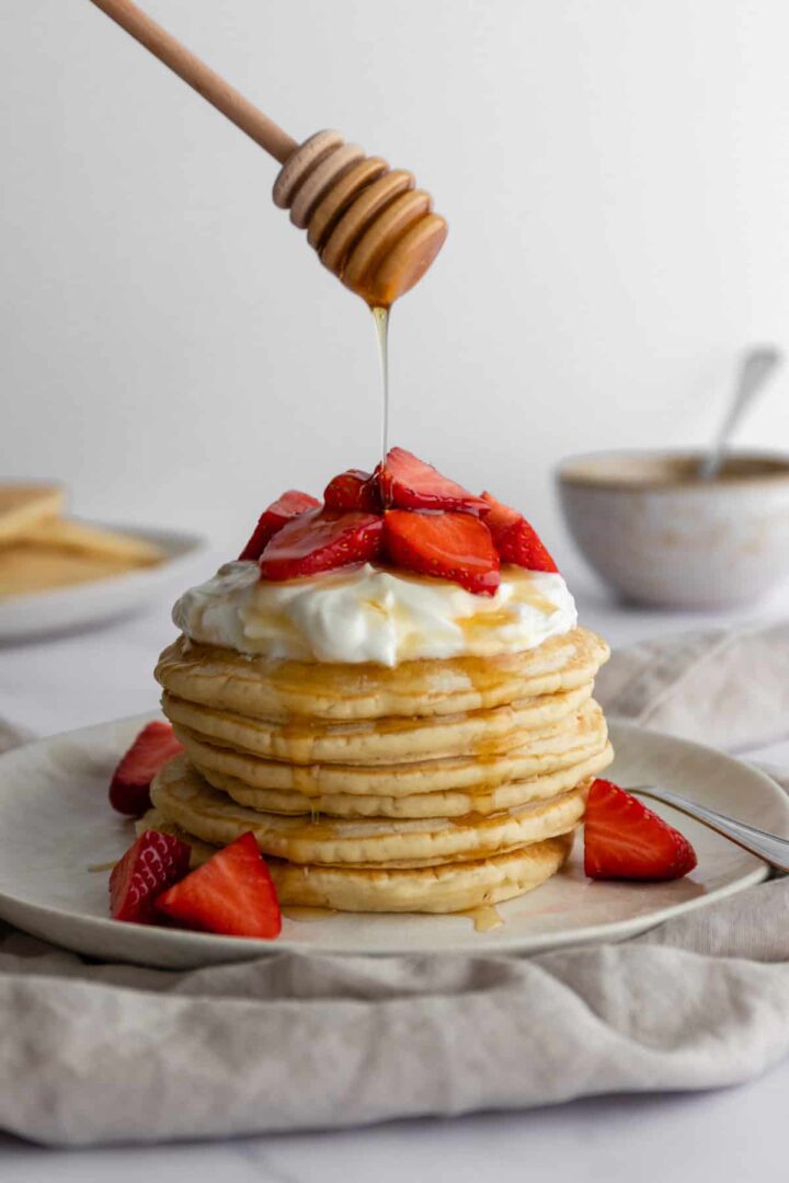 a plate with a stack of vegan pancakes with coconut yogurt, strawberries and maple syrup on top