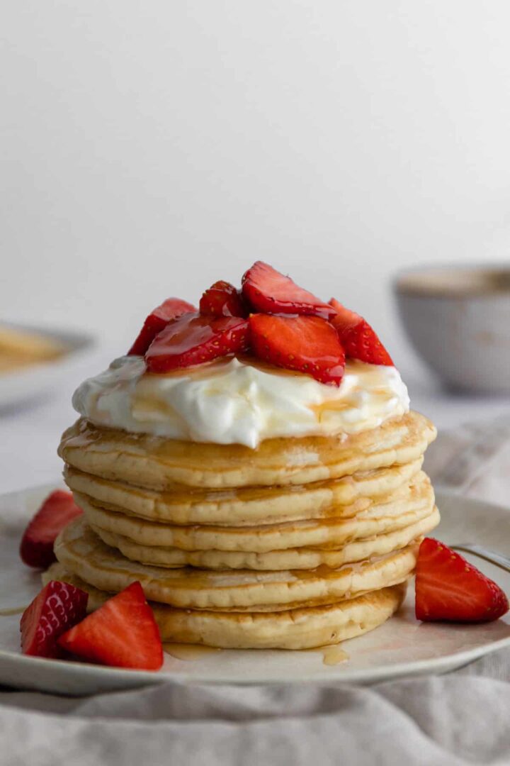 close up stack of pancakes with coconut yogurt, strawberries and maple syrup on top