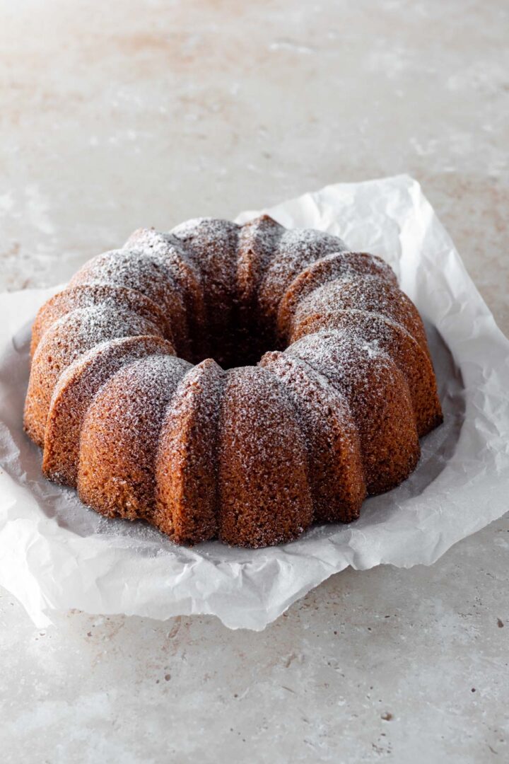 a bundt carrot cake with powdered sugar on top, on top of white parchment paper on a beige board