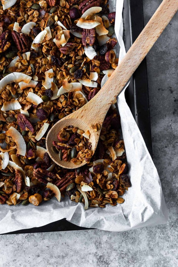 granola on a baking tray with a wooden spoon