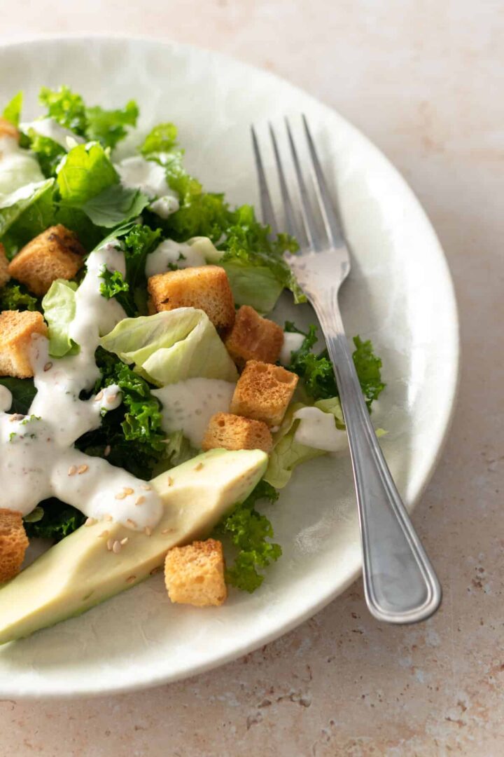 close up of a kale caesar salad served on a plate and a fork on the side
