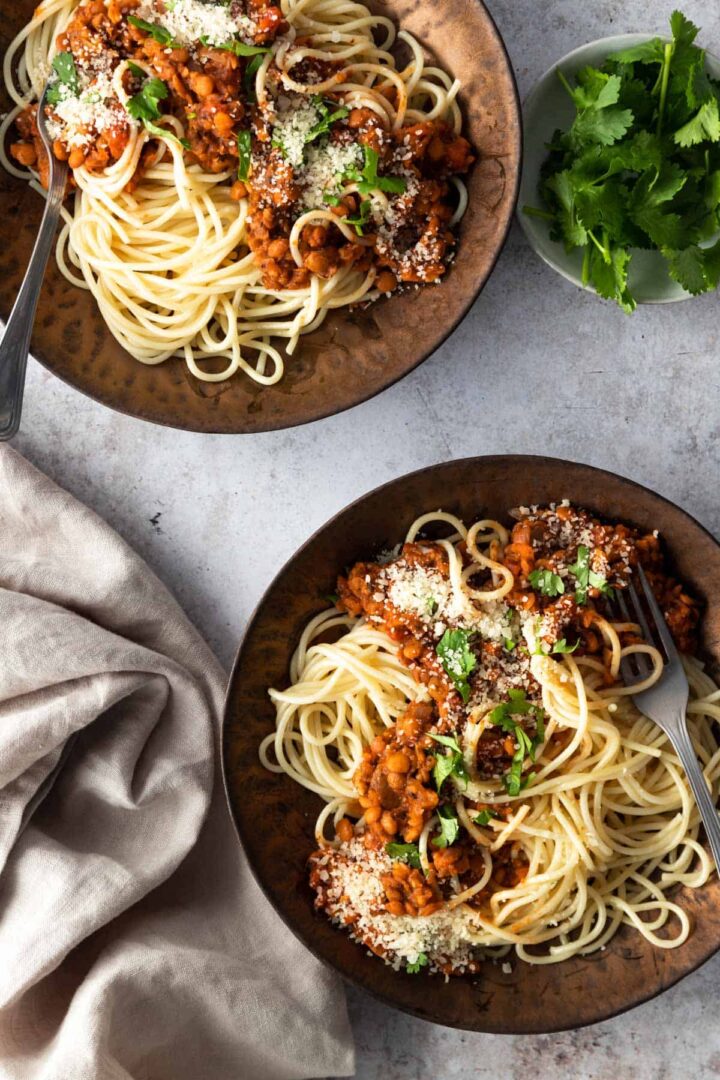 two bowls with spaghetti, lentil and tomato sauce, grated parmesan and coriander. A small bowl with coriander on the side