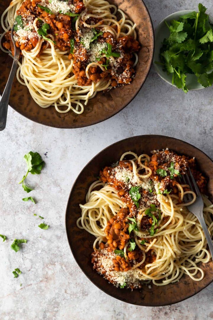 two bowls with spaghetti, lentil and tomato sauce, grated parmesan and coriander. A small bowl with coriander on the side