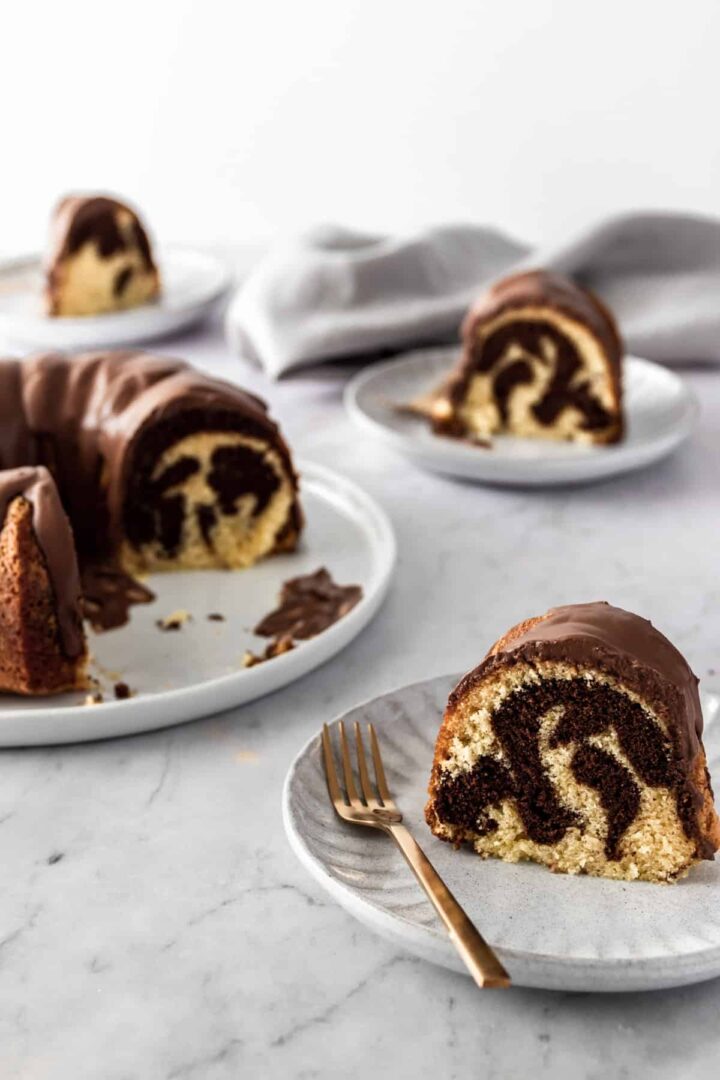 A big plate with a marble cake and three small plates with one cake slice each