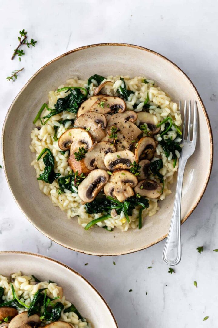 a plate with mushroom risotto with spinach, garnished with thyme and a fork on the side