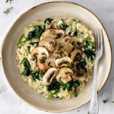 a plate with mushroom risotto with spinach, garnished with thyme and a fork on the side