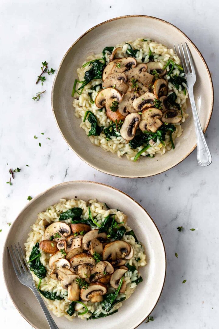 two plates with arborio rice, mushrooms, spinach, garnished with thyme and a fork on the side