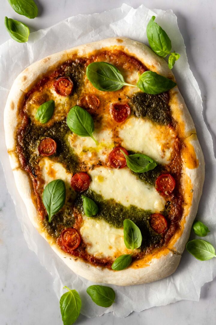 pizza with mozzarella, tomato sauce, pesto sauce, cherry tomatoes and basil leaves