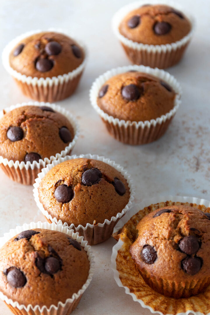 seven muffins with chocolate chips on top of a beige board