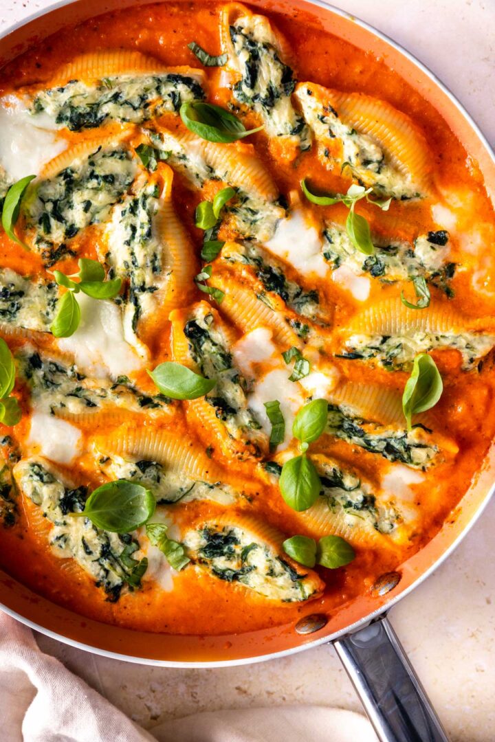 close up of a skillet with tomato sauce, pasta shells stuffed with ricotta with basil leaves on top
