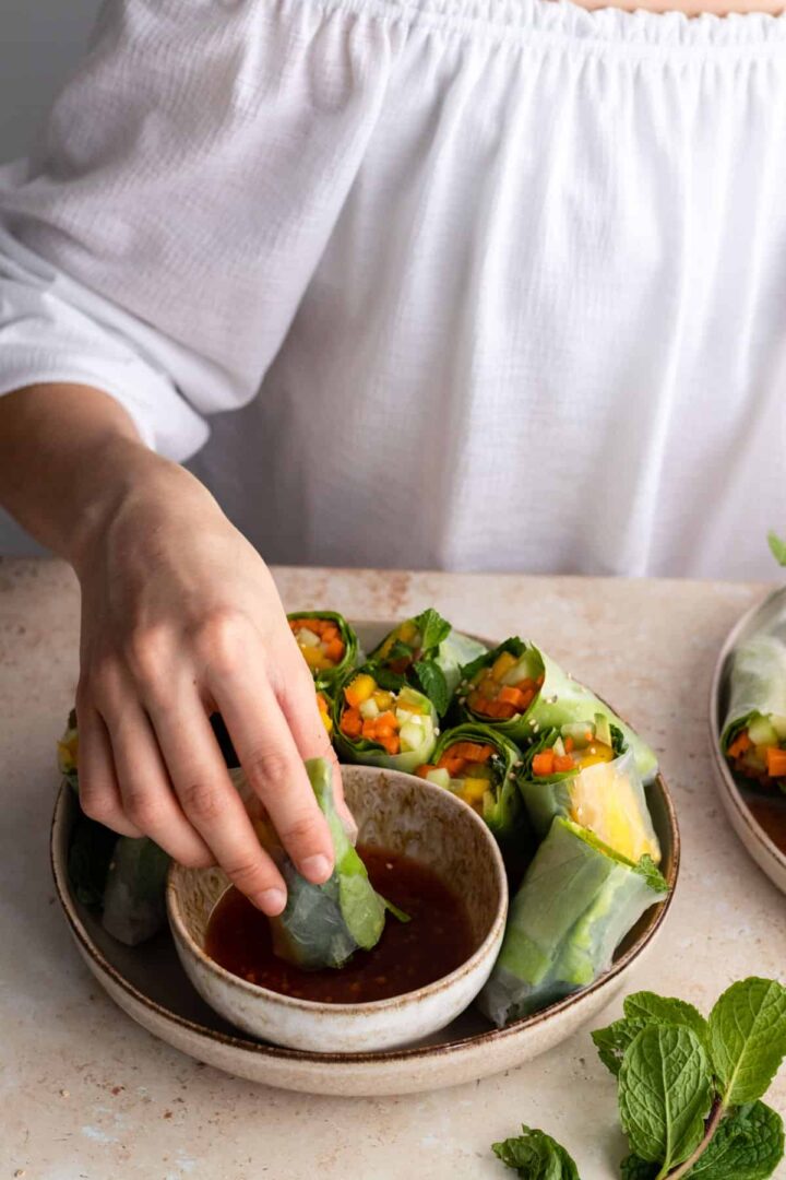 Rita dipping a spring roll into a bowl with sweet chili sauce