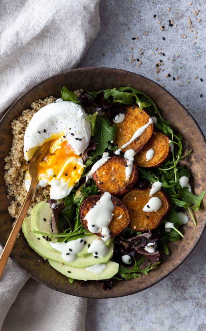 close up bowl with quinoa, avocado, sweet potato, mixed greens, white dressing and sesame seeds on top