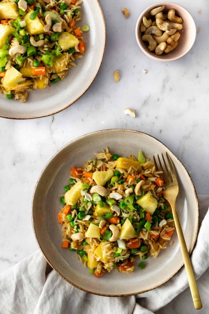 Thai pineapple fried rice served on two plates and a bowl with cashews on the side