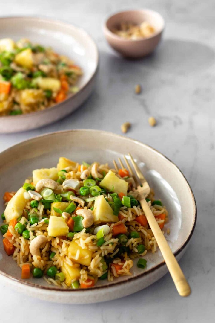 Thai pineapple fried rice served on two plates and a bowl with cashews on the side