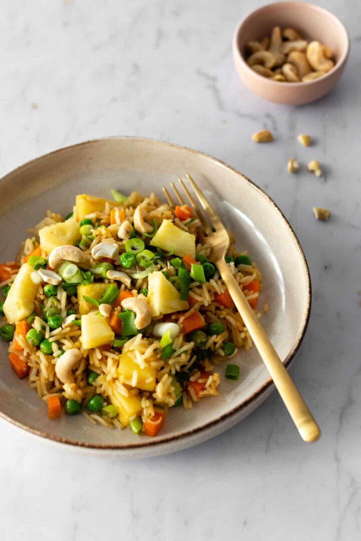 Thai pineapple fried rice served on a plate and a bowl with cashews on the side