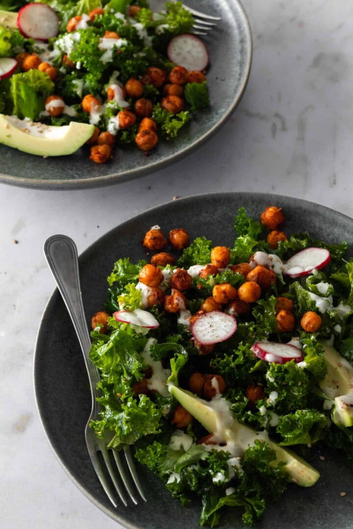 two plates with massaged kale salad on top of a marble table