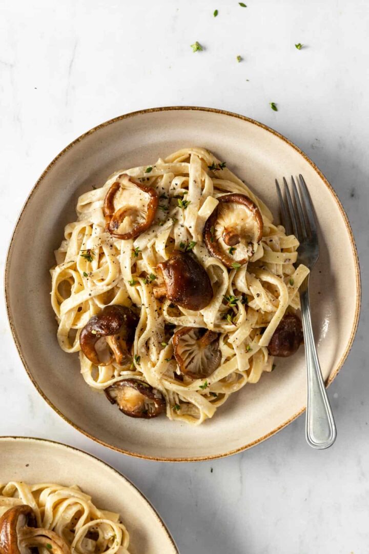 Shiitake mushrooms and fettuccine pasta served on a plate with fresh thyme on top