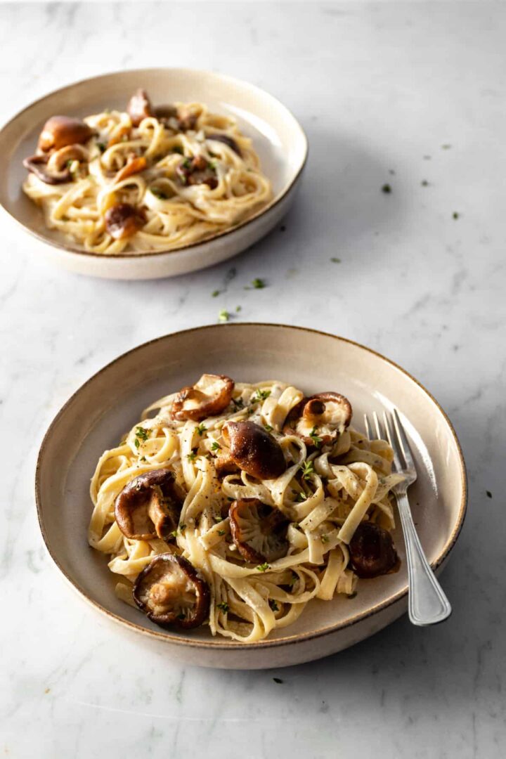 Two plates served with shiitake mushrooms, fettuccine pasta, and garnished with fresh thyme on top