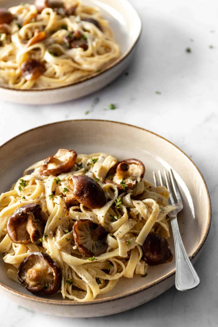 Shiitake mushrooms and fettuccine pasta served on a plate and garnished with fresh thyme