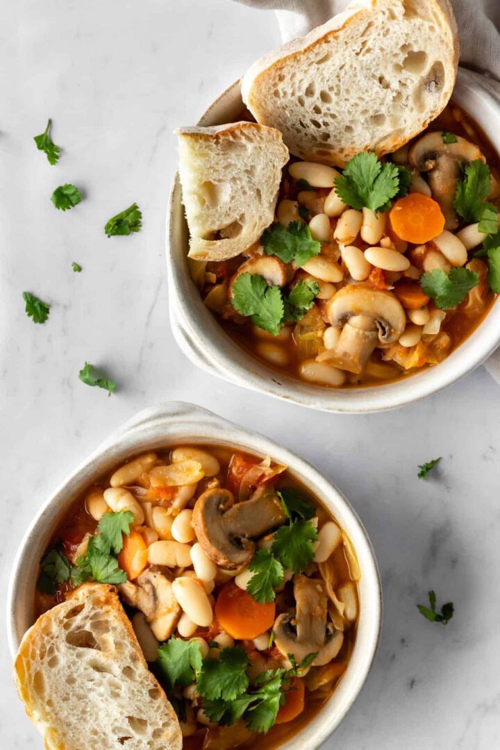 two bowls with mushrooms, carrots, white beans, coriander and sliced bread on the sides