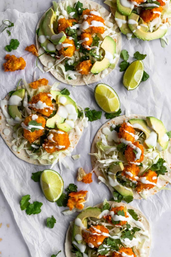 cauliflower tacos on top of parchment paper, garnished with coriander, lime wedges and cream sauce
