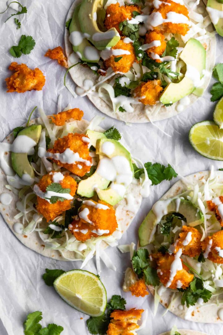 cauliflower tacos on top of parchment paper, garnished with coriander, lime wedges and cream sauce