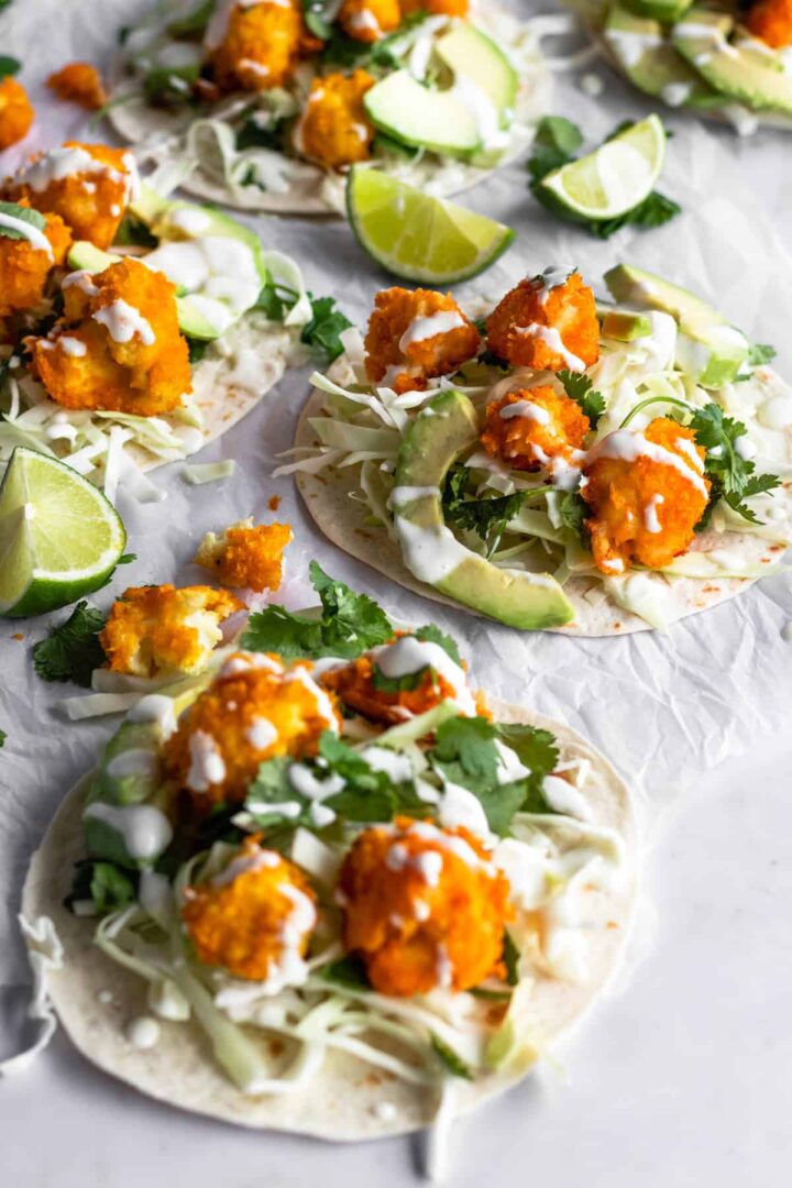 cauliflower tacos on top of parchment paper, garnished with coriander, lime wedges and cream sauce