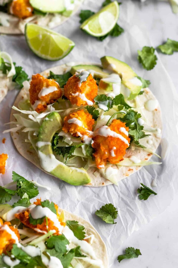 cauliflower tacos on top of parchment paper, garnished with coriander, lime wedges and cream sauce