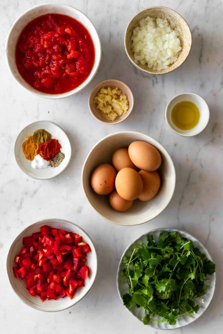 ingredients to make shakshuka: spices, onion, olive oil, garlic, canned tomato, eggs, bell pepper, coriander