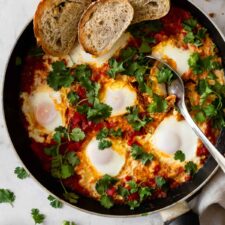 a kitchen pan with shakshuka garnished with coriander and toasted sliced bread on the side