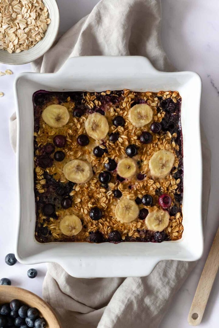 a baking dish served with blueberry baked oatmeal with a small bowl with oats on the side and another bowl with blueberries
