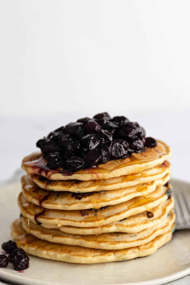 a plate with a stack of pancakes, blueberries and maple syrup on top