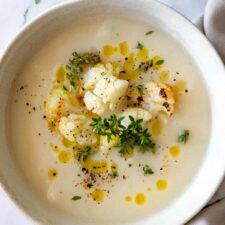 a bowl served with soup and garnished with roasted cauliflower, olive oil, thyme and black pepper