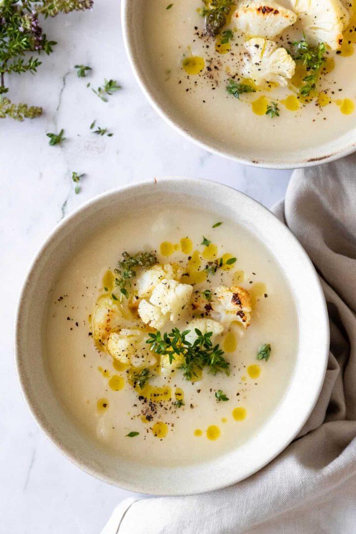 two bowls served with soup and garnished with roasted cauliflower, olive oil, thyme and black pepper