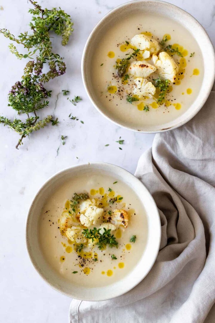 two bowls served with soup and garnished with roasted cauliflower, olive oil, thyme and black pepper