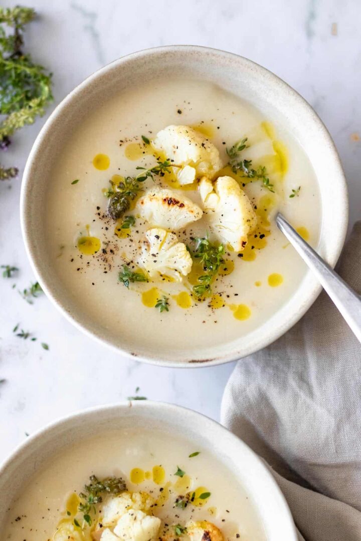 two bowls served with soup and garnished with roasted cauliflower, olive oil, thyme and black pepper