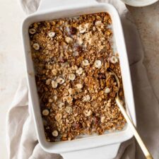 pumpkin baked oatmeal on a baking dish with a gold spoon on the side. A small bowl with paçoca on the top right corner