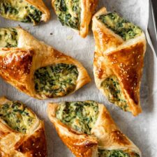 spinach puffs garnished with sesame seeds on top of parchment paper