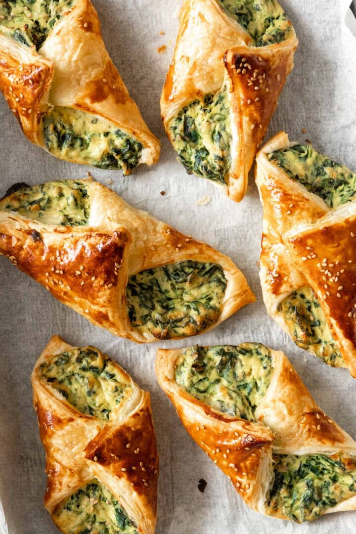 spinach puffs garnished with sesame seeds on top of parchment paper