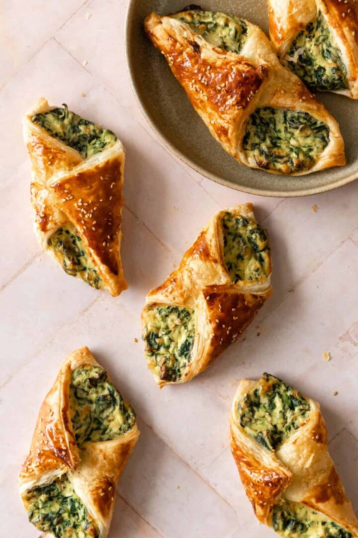 a plate with two spinach puffs and more spinach puffs on top of a pink board