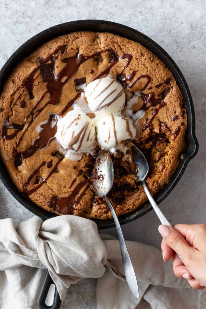 chocolate chip skillet cookie with vanilla ice cream on the top and two spoons