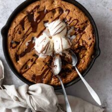 a black skillet with chocolate chip cookie and three ice cream balls on top and chocolate topping