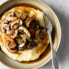 a plate served with mashed potatoes, sliced mushrooms, carrots and garnished with chopped chives