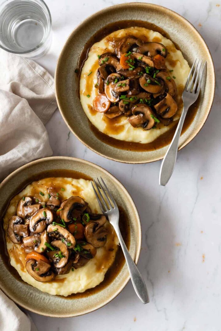 two plates served with mashed potatoes and mushroom bourguignon. A glass with water on the side