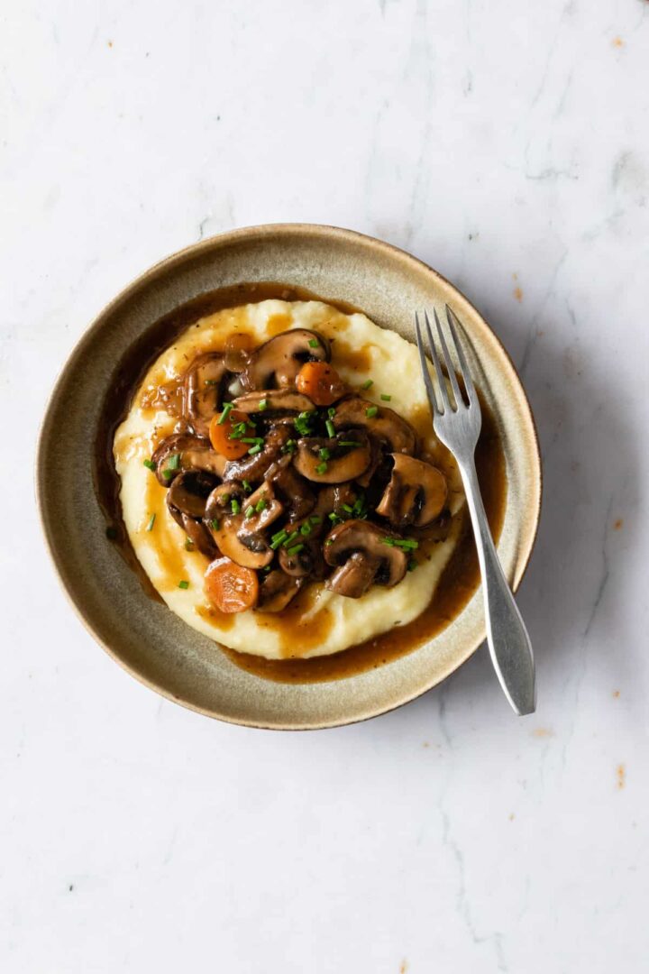 a plate served with mushroom bourguignon garnished with chopped chives on a marble table