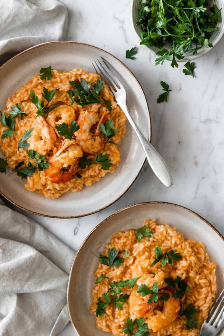 two plates served with arborio rice, shrimp and parsley. A small bowl with parsley on the side.
