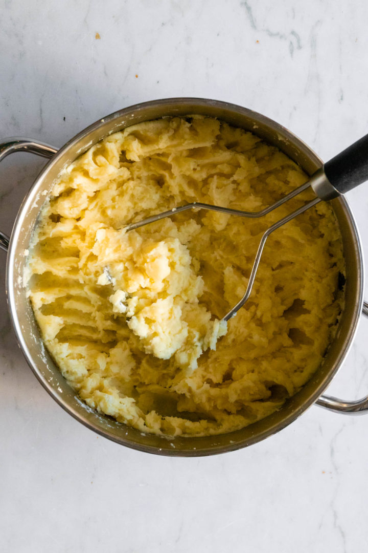 a cooking pot with mashed potato and a potato masher