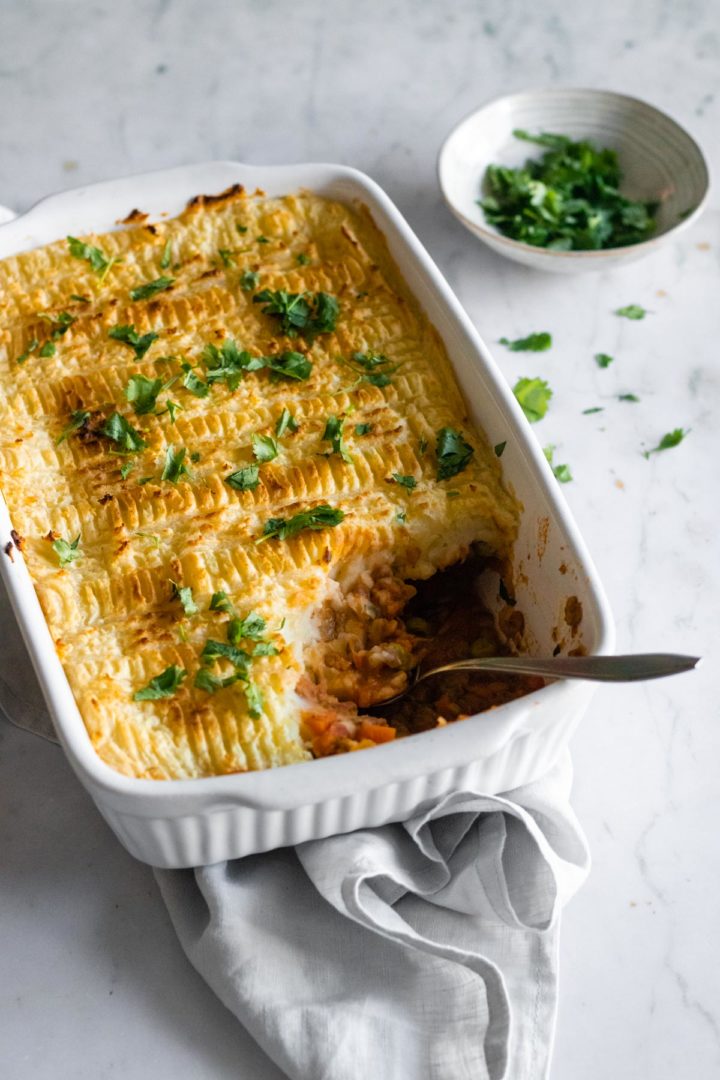 a baking dish with lentil Shepherd's pie, chopped coriander and a spoon. A small bowl with chopped coriander on the side